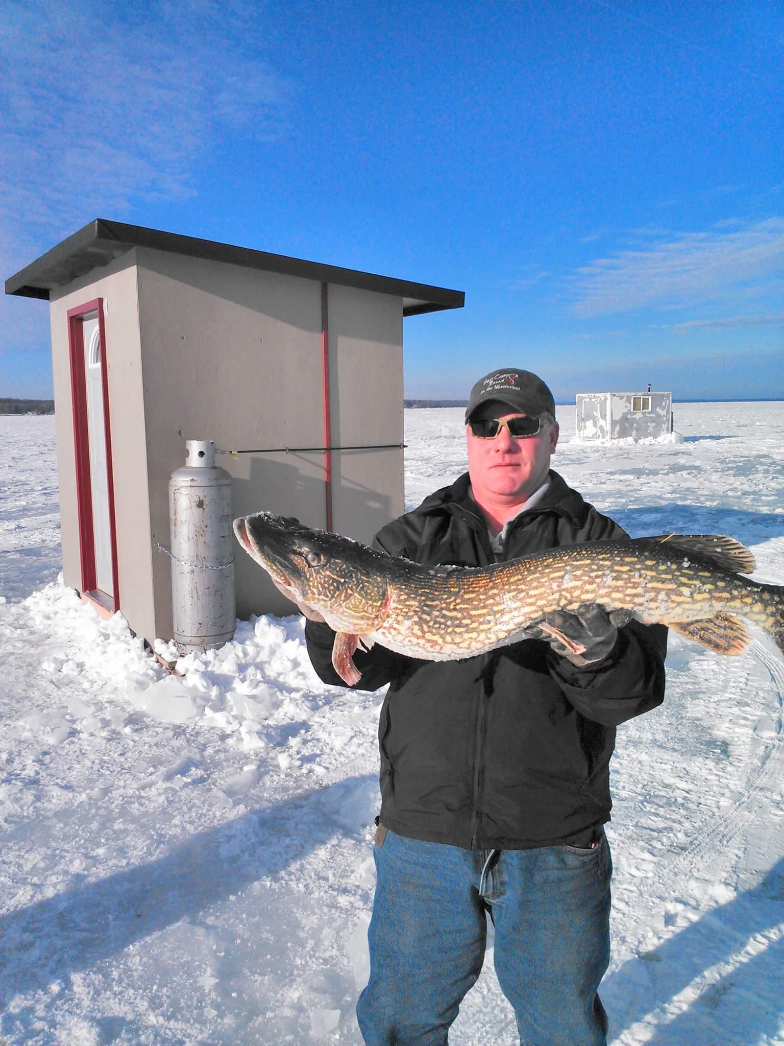 Man with Fish In front of Ice Fishing Houses
